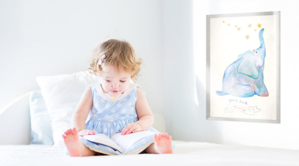 Baby girl sitting on bed reading. Good Luck print customized with her name is on the wall.