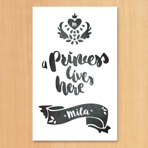 A Black & White print with a royal crest and text "A Princess Lives Here". Set your girl's initial in the heart inside the crest and her name in the decorative banner below.